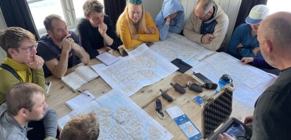 Polar explorer Jim McNeill leads an Ocean warrior planning meeting. A group poring over maps. Join the adventure through Classic Sailing