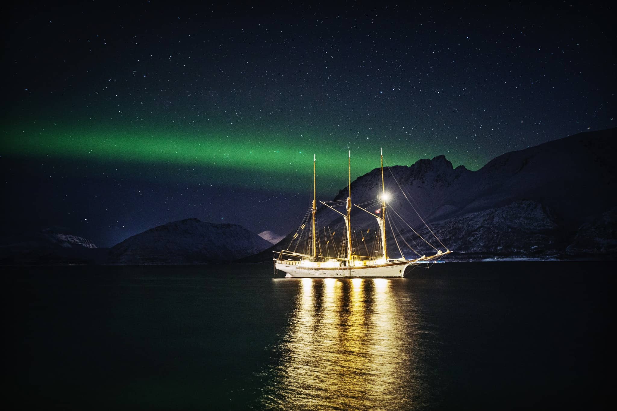 Sailing ship Linden at anchor in Svalbard, with a starry sky and the green glow of the Northern Lights.