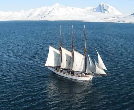 Linden on a sailing and scientific expedition in Svalbard. Sailing in the sunshine with a snowy landscape behind. Join her through Classic Sailing